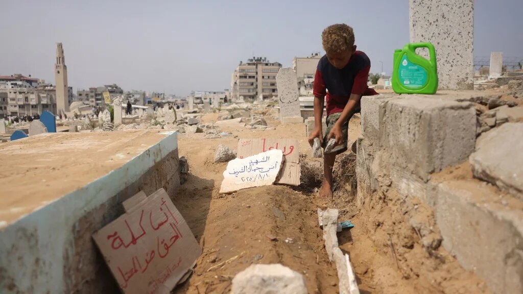 A Palestinian boy adjusts stones around the grave of Al Jazeera's Anas al-Sharif, who was killed alongside other journalists in an Israeli strike, in Gaza City on 12 August 2025 (Bashar Taleb/AFP)