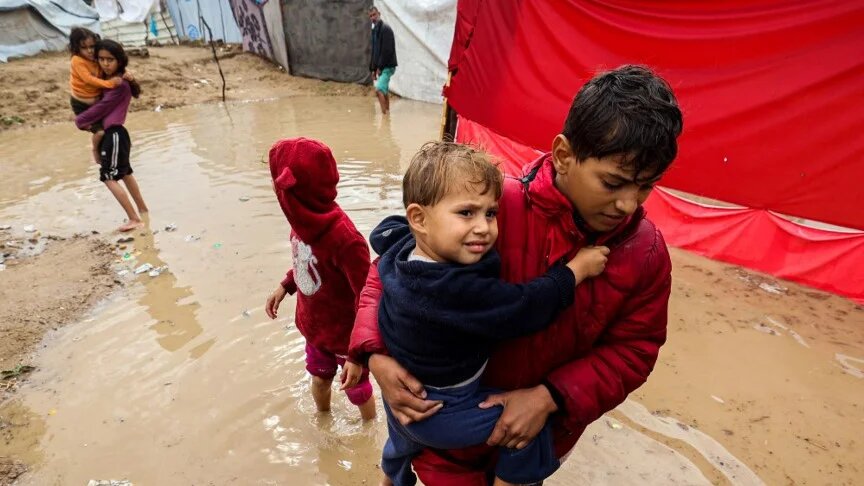 Palestinian children walk in floodwaters after heavy rains in Maghazi refugee camp, in the central Gaza Strip, on 25 November 2025 (Eyad Baba/AFP)