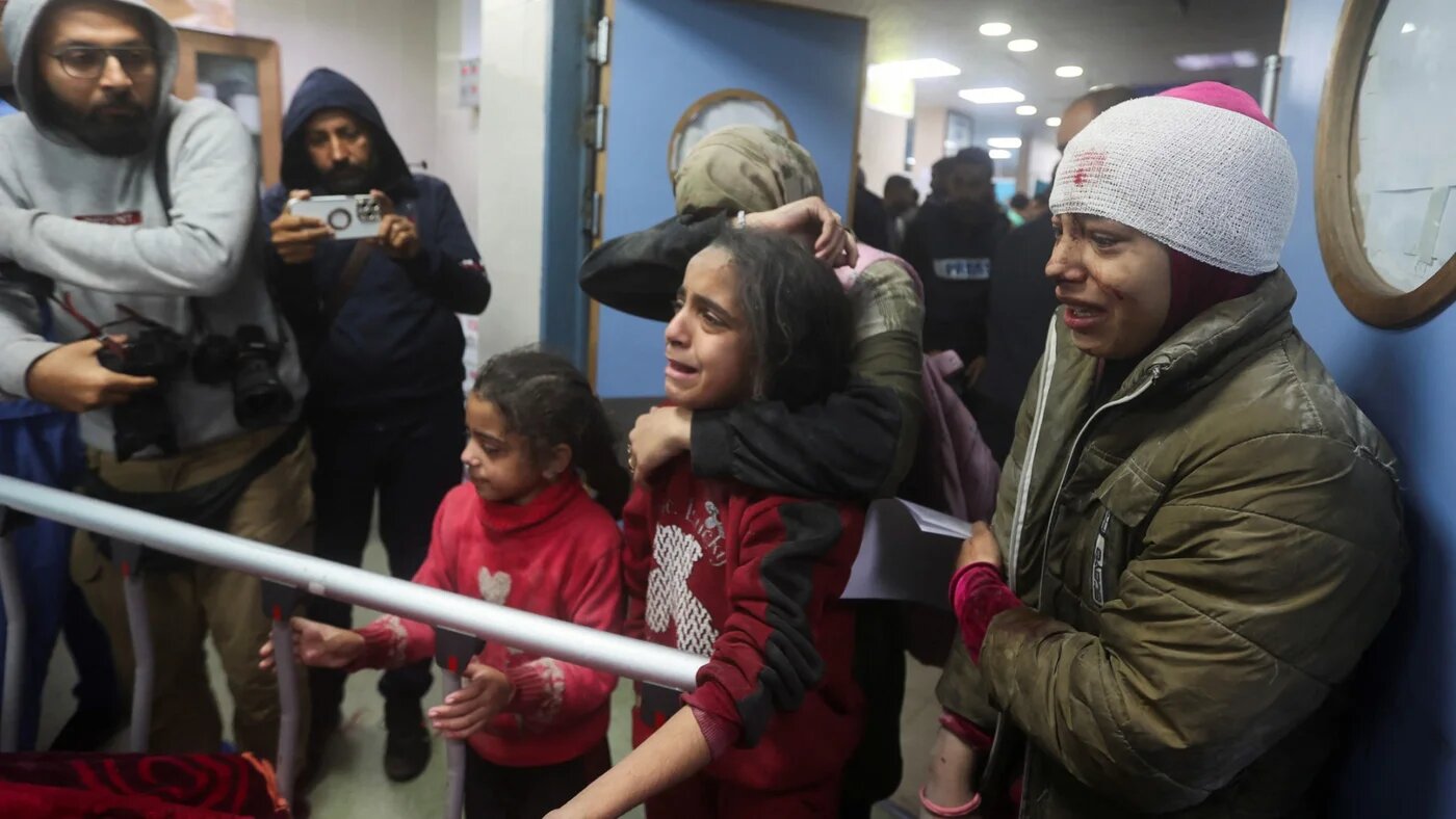 People react next to the bed of a Palestinian wounded in an Israeli strike at a hospital in Khan Younis on 28 December 2023 (Ahmed Zakot/Reuters)