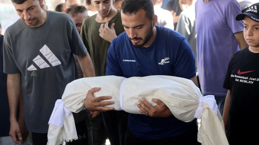 A mourner carries the shrouded body of an infant killed in an overnight Israeli airstrike at al-Shifa Hospital in Gaza City, on 2 August 2026 (Omar al-Qattaa/AFP)
