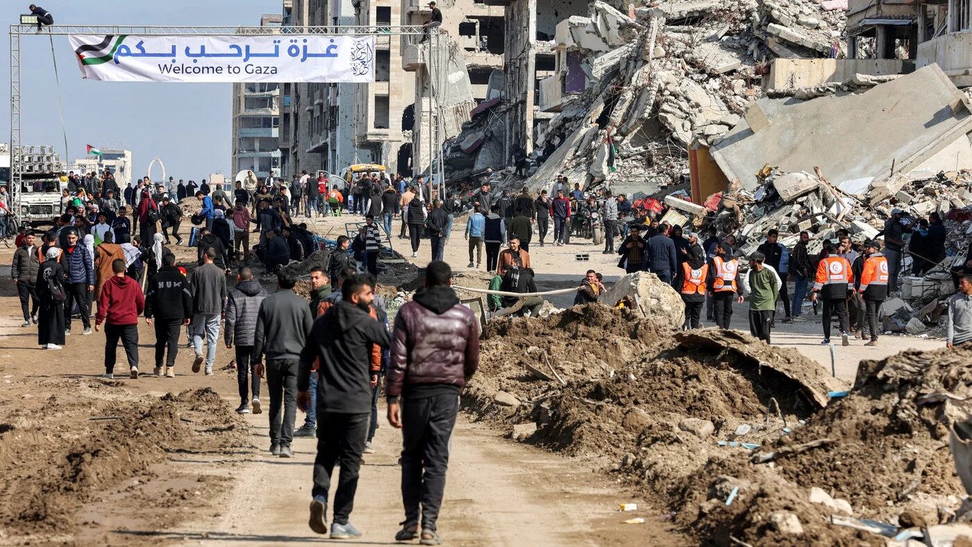 Palestinians walk past a banner welcoming people along Rasheed Street into Gaza City on 26 January 2025 (Omar Al-Qattaa/AFP)