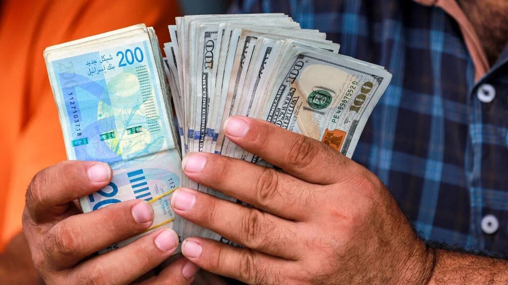 A man counts stacks of Israeli shekels and US dollars at an informal money exchange stall in Deir al-Balah, in the central Gaza Strip, on 2 July 2024 (Bashar Taleb/AFP)