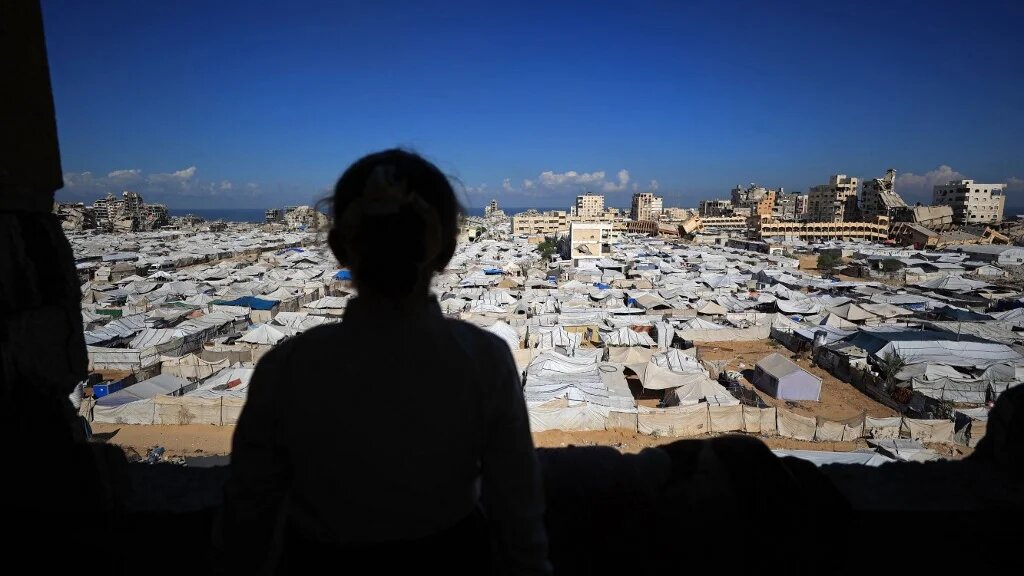 A girl looks at the temporary tents of displaced Palestinians, alongside destroyed buildings, in Gaza City on 7 October 2026 (Omar al-Qattaa/AFP)