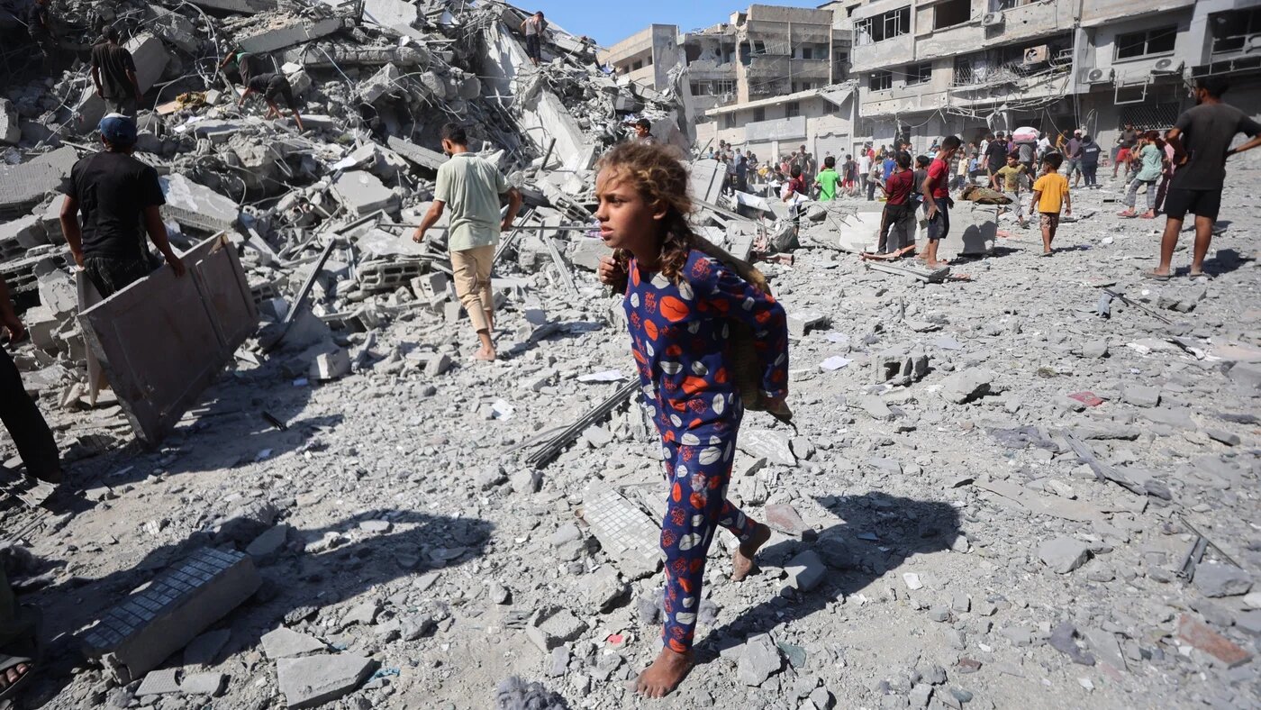 A barefoot Palestinian girl can be seen near the rubble of al-Ghafari tower in Gaza City after it was destroyed by Israeli air strikes on 15 September 2025 (Omar al-Qattaa/AFP)