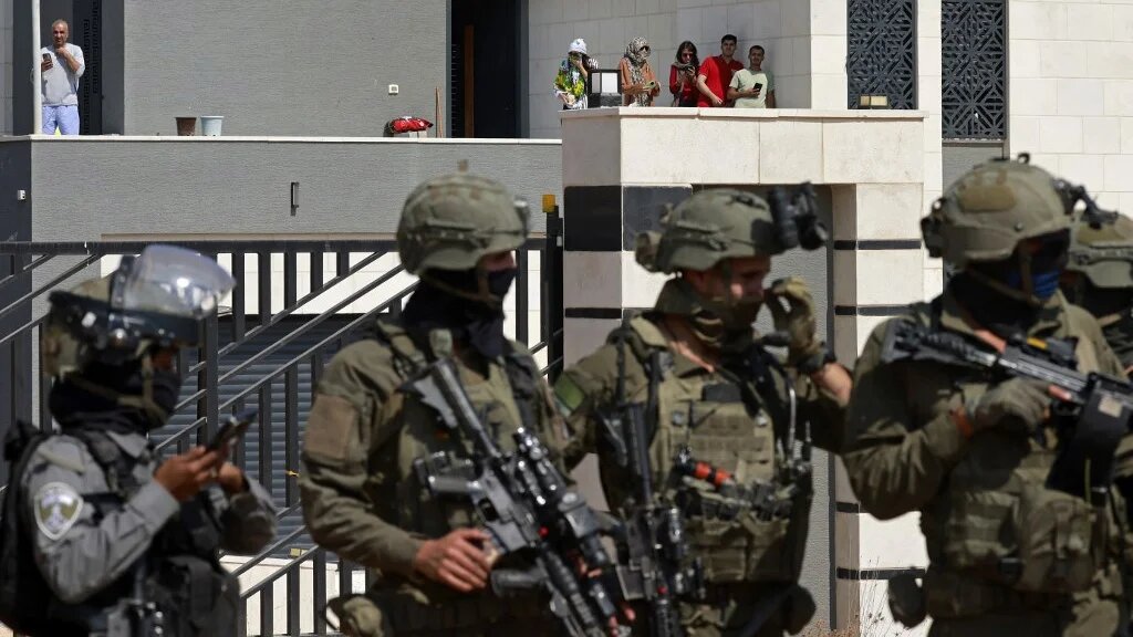 Israeli soldiers stand by the entrance of a Palestinian house besieged by settlers in the village of Qusra, in the occupied West Bank, on 14 August 2026 (Jaafar Ashtiyeh/AFP)