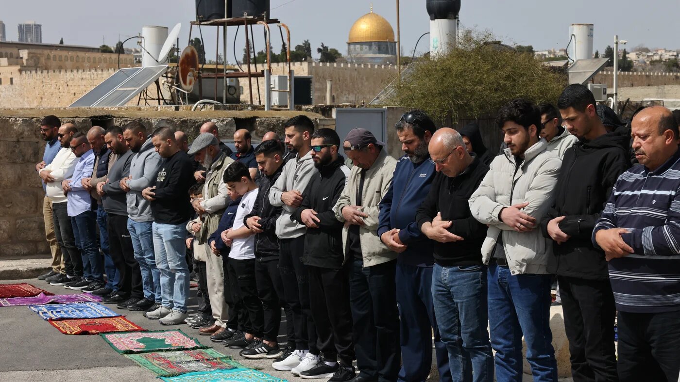 Palestinian Muslim worshippers attend prayers by a road, as they are not permitted to enter Al-Aqsa Mosque complex amid Israeli restrictions, in Jerusalem on 13 March 2026 (Ammar Awad/Reuters)