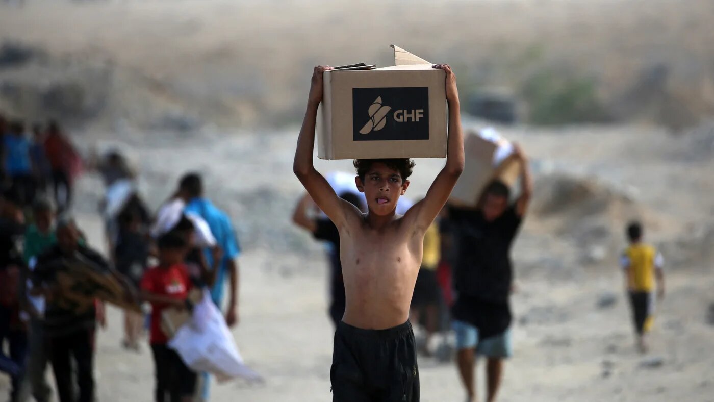 A Palestinian boy carries a box as people return from a food distribution point run by the US and Israeli-backed Gaza Humanitarian Foundation (GHF) group, near the Netsarim corridor in the central Gaza Strip on 5 October 2025 (AFP)