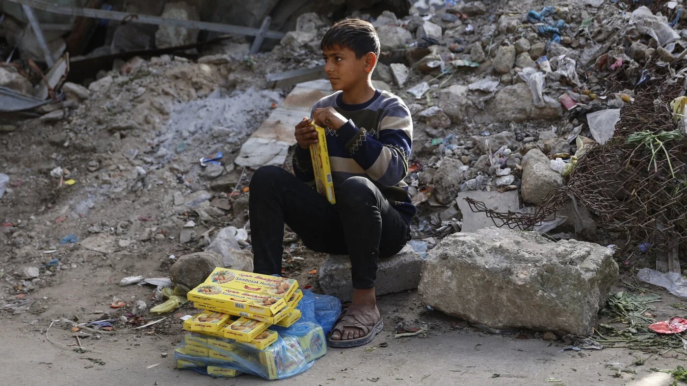 A Palestinian child sits on the rubble in Gaza City's Zawiya market on 18 February, 2026 (AFP/Omar aL-Qattaa)