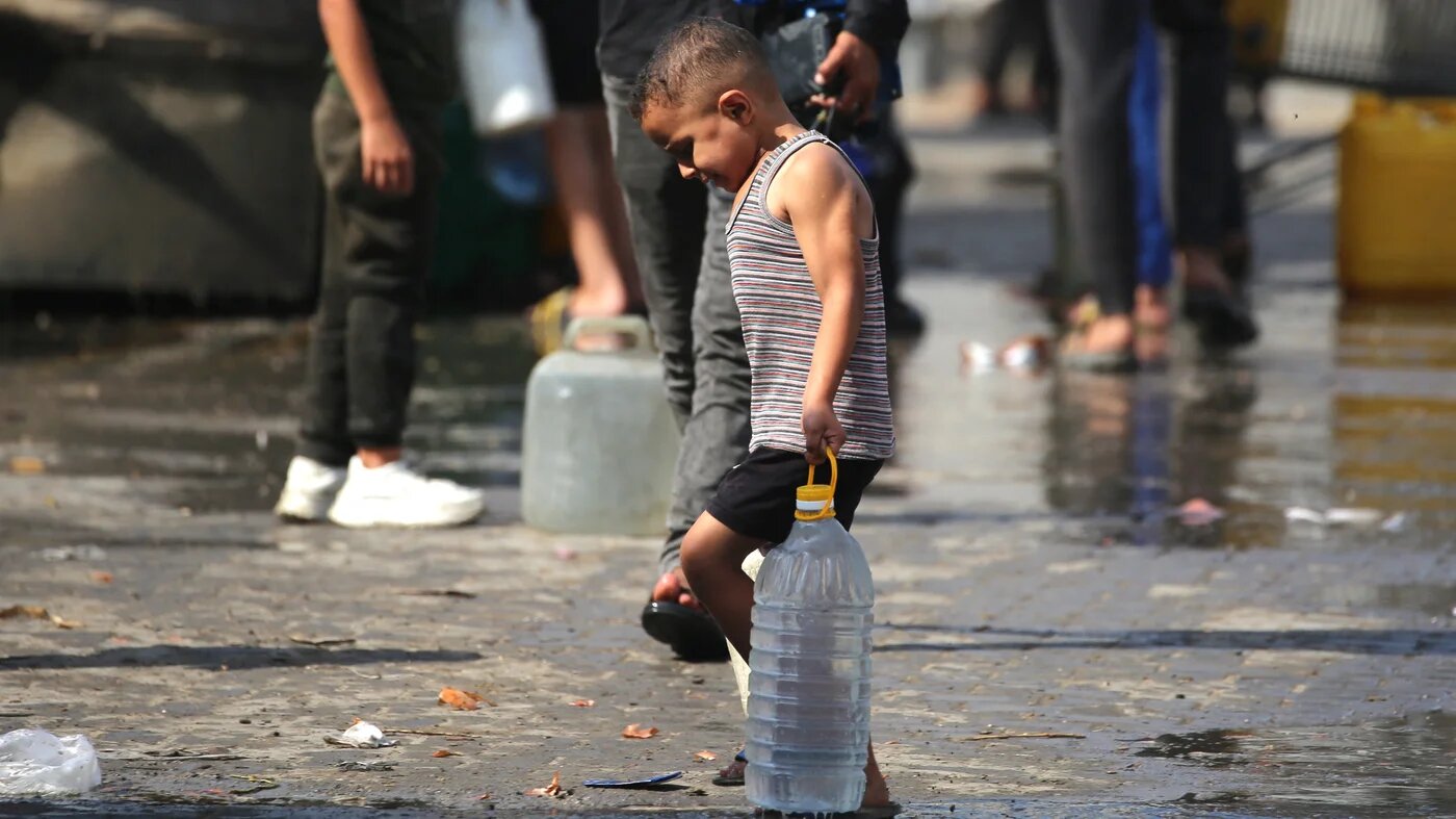 A Palestinian child carries a large plastic bottle filled with water in the Nuseirat refugee camp, central Gaza Strip, on 2 November, 2025 (Eyad Baba)