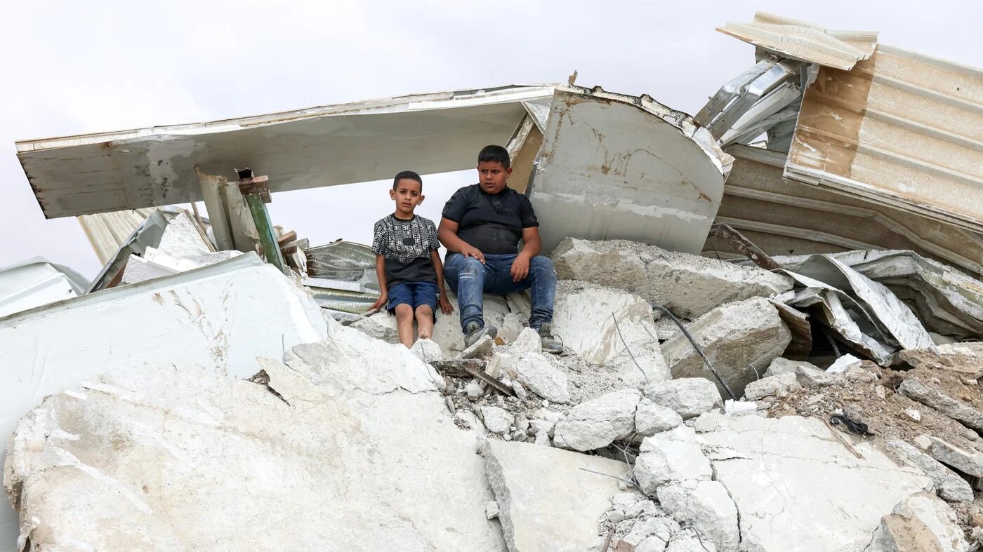 Children sit on top of the rubble of a building demolished by Israeli forces near the city of Rahat on 12 October 2026 (Ahmad Gharabli/AFP)
