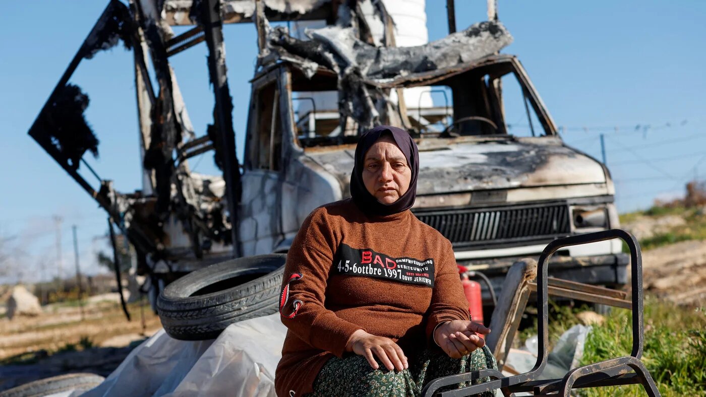 A Palestinian woman sits near a vehicle burned by Israeli settlers in Susiya, occupied West Bank, on 25 February 2026 (Reuters/Mussa Qawasma)