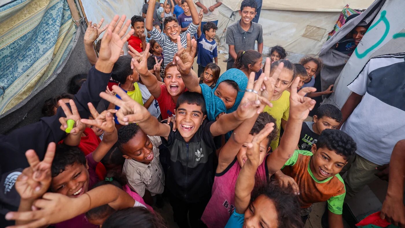 Palestinians celebrate the ceasefire deal announcement at a camp for displaced people in Nuseirat, central Gaza Strip on 9 October 2025 (AFP/Eyad Baba)