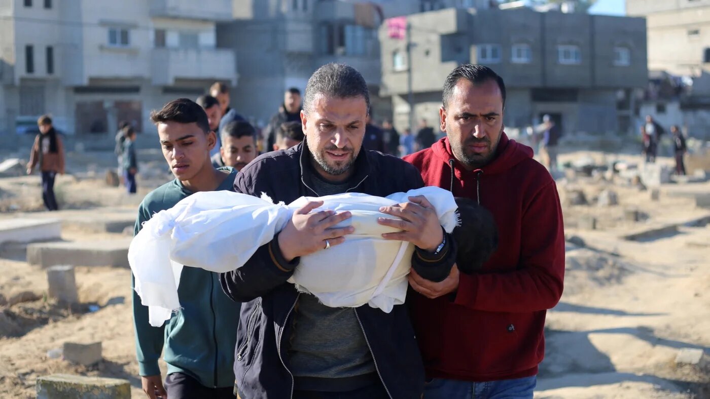 A Palestinian man carries the body of a child killed in an Israeli strike during a funeral in Deir al-Balah, central Gaza Strip, on 15 December 2024 (Eyad Baba/AFP)