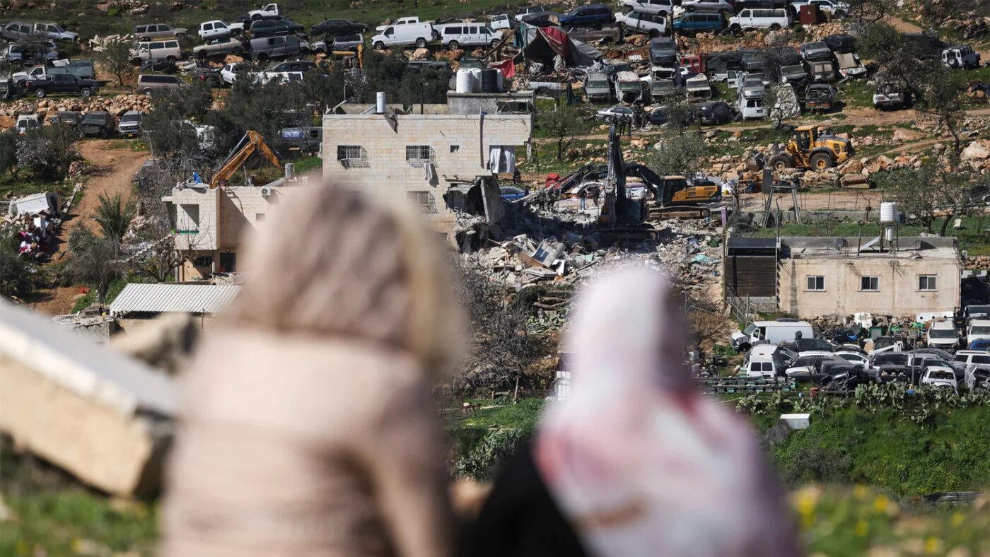 Palestinian women look on as Israeli bulldozers demolish an apartment building near the Israeli settlement of Hagai, south of the occupied West Bank city of Hebron, 18 February 2026 (AFP)