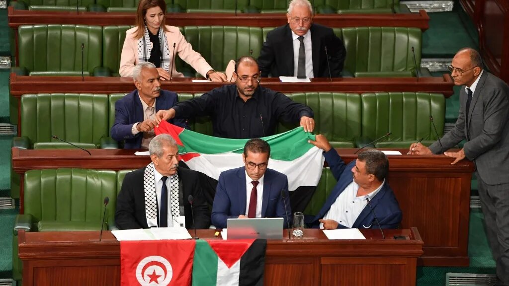 Des parlementaires tunisiens déplient le drapeau palestinien lors d’une minute de silence pour les victimes palestiniennes de Gaza, à l’ouverture d’une séance consacrée à un projet de loi sur la criminalisation de la normalisation avec Israël, le 2 novembre (AFP/Fethi Belaïd)