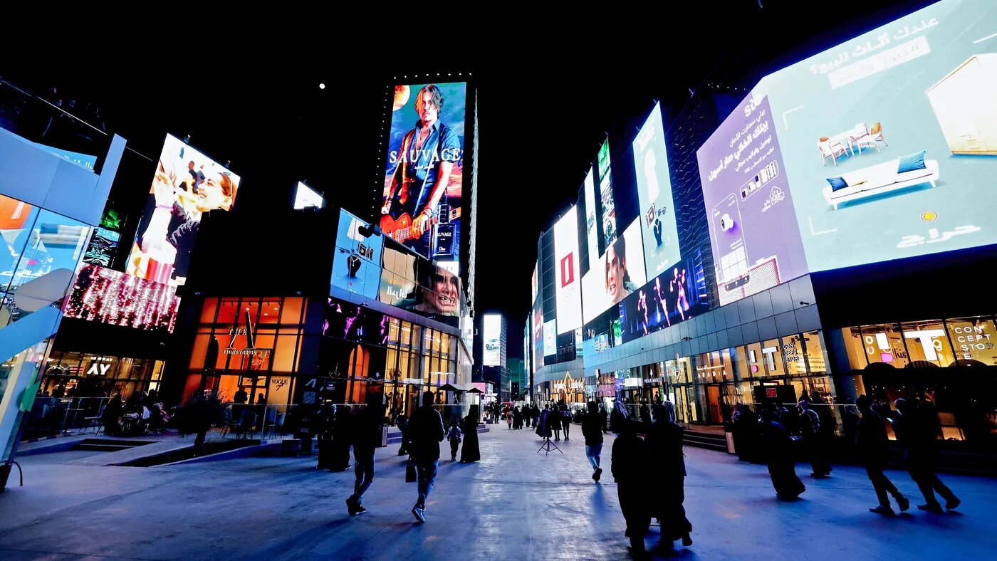 People walk beneath advertisement billboards at Boulevard entertainment city in the Saudi capital Riyadh, late on 19 January 2022 (AFP/Fayez Nureldine)
