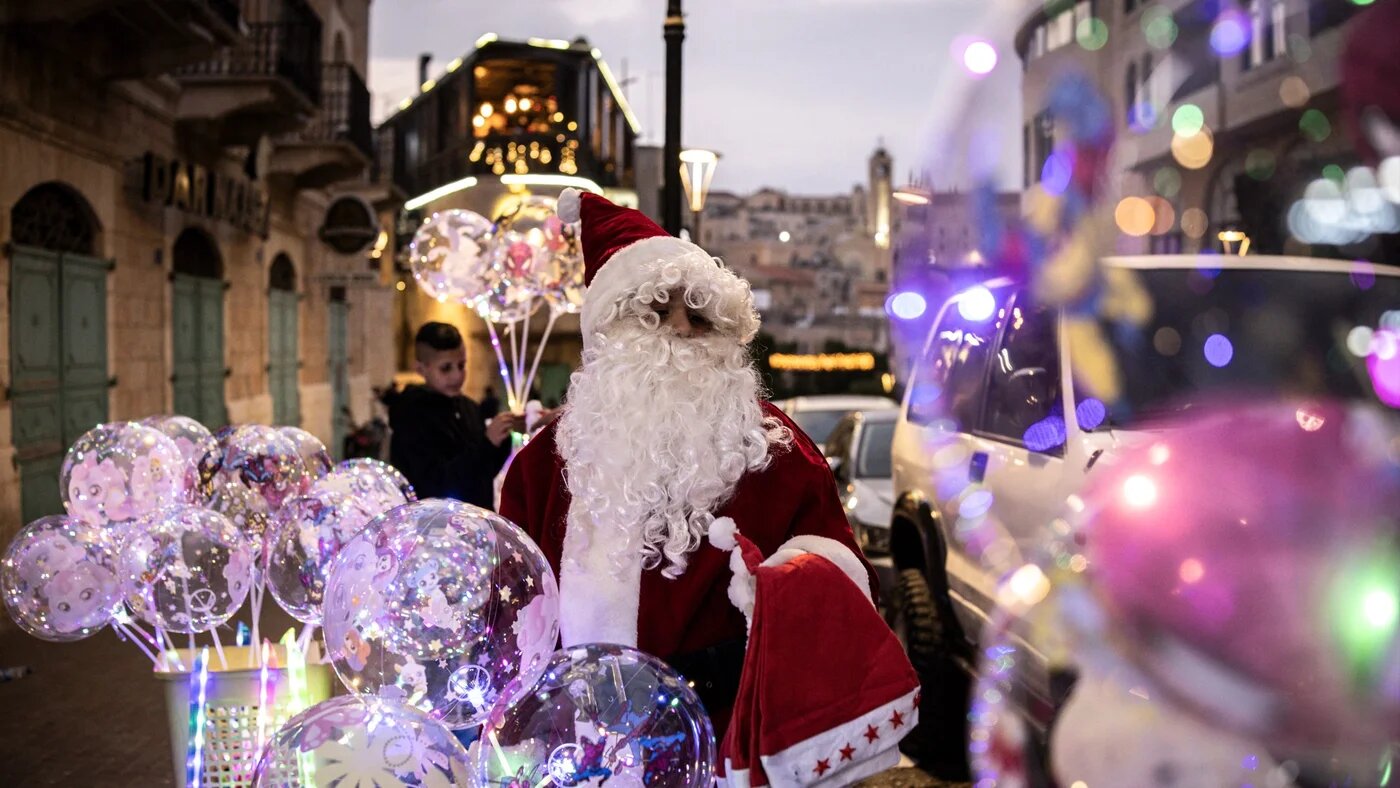 A man dressed as Santa Claus sells balloons near Nativity Square during a Christmas tree lighting ceremony in Bethlehem, in the Israeli-occupied West Bank, on 6 December 2025 (John Wessels/AFP)