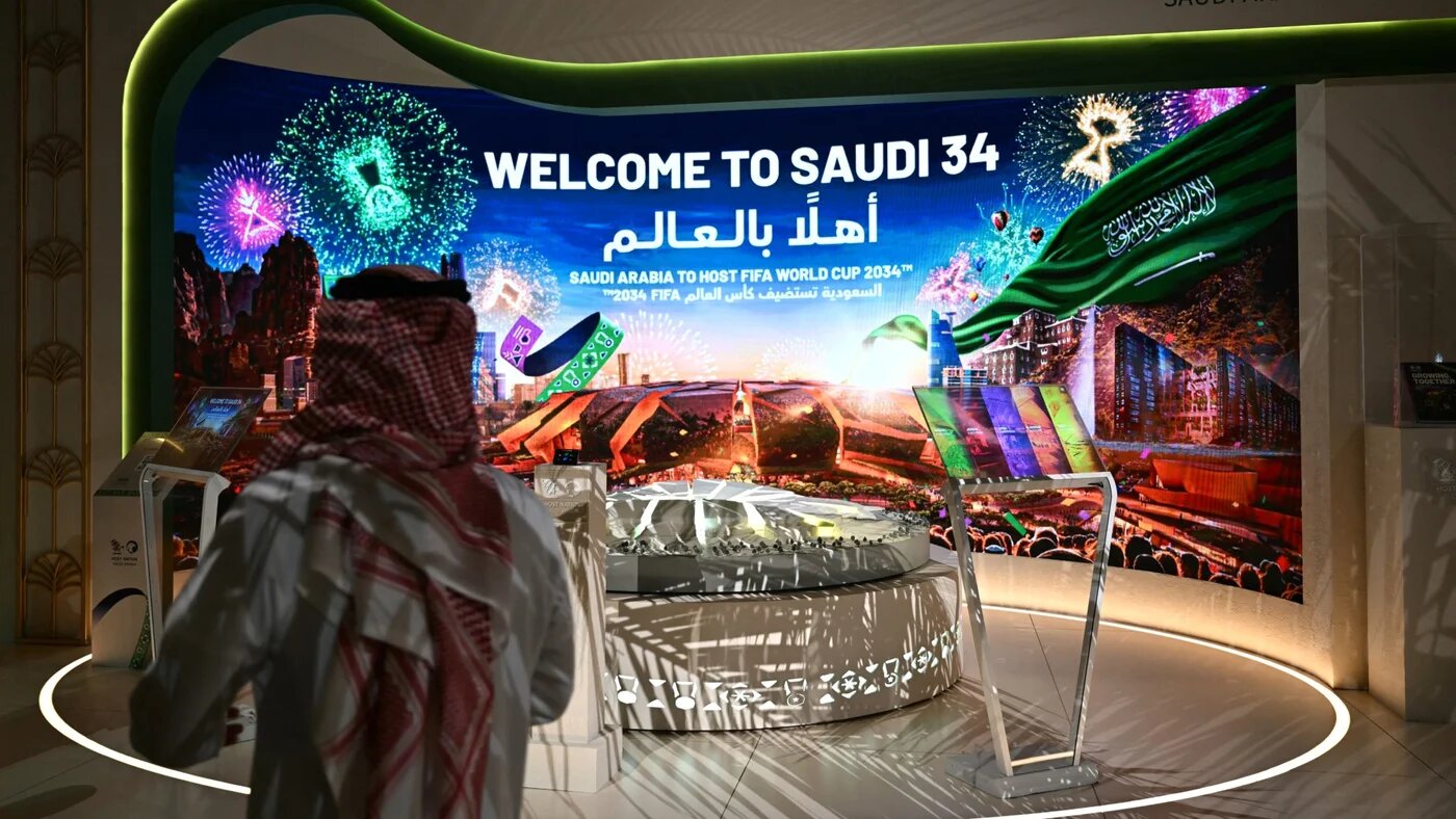 A man walks past a stall displaying a welcome message for the Saudi 2034 FIFA World Cup football tournament at the Ministry of Media in Riyadh on 13 May 2025 (AFP/Giuseppe Cacace)