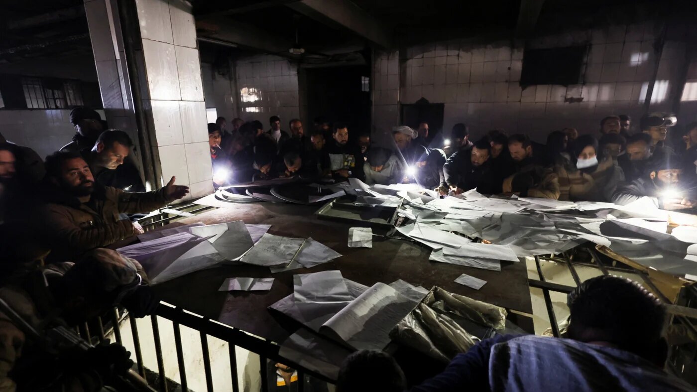 People search through papers as they join members of the Syrian civil defence group, known as the White Helmets, to search for prisoners underground at Sednaya prison on 9 December 2024 (Amr Abdallah Dalsh/Reuters)