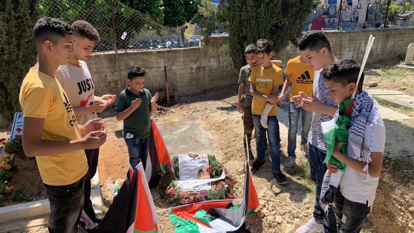 Friends of Islam Burnat recite a prayer for him at his grave. Burnat was shot dead by Israeli forces.