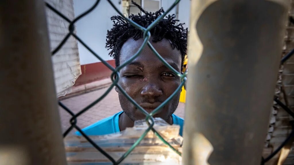 A Sudanese migrant looks through a fence in a temporary centre for migrants and asylum seekers on June 25, 2022 in Melilla (AFP)