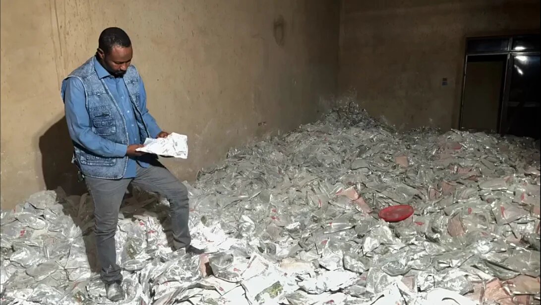 An official with Sudan’s General Intelligence Service examines one of thousands of packets of captagon at a factory in al-Jaili  area (Sudan News/X screengrab)