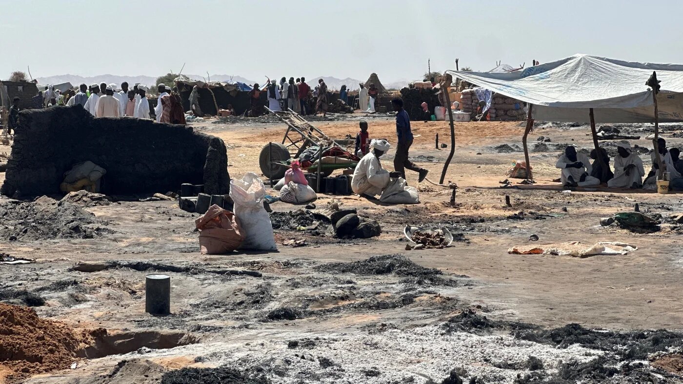 Displaced Sudanese people who left El-Fasher after its fall, sit in the shade in Tawila amid the remains of a fire that broke out in the camp on 11 February 2026 (AFP)