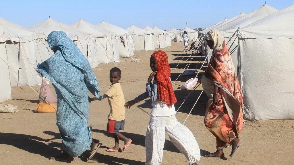 People displaced from Sudan’s el-Fasher walk past tents at al-Afad camp in the country’s north, on 15 November 2025 (Ebrahim Hamid/AFP)