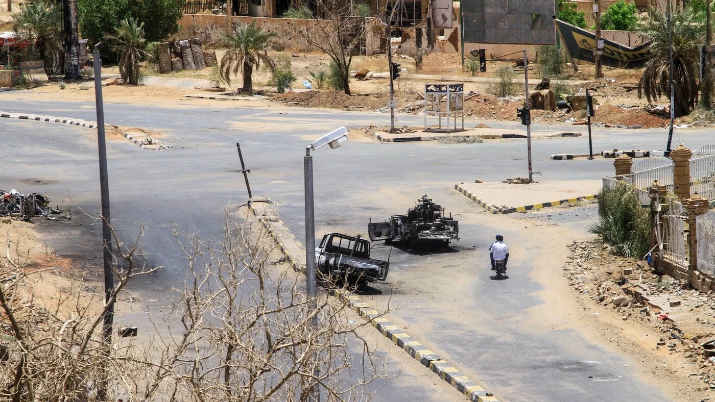 Sudanese men ride on a motorcycle past destroyed military vehicles in front of a hospital in Khartoum on 28 April 2025 (AFP)