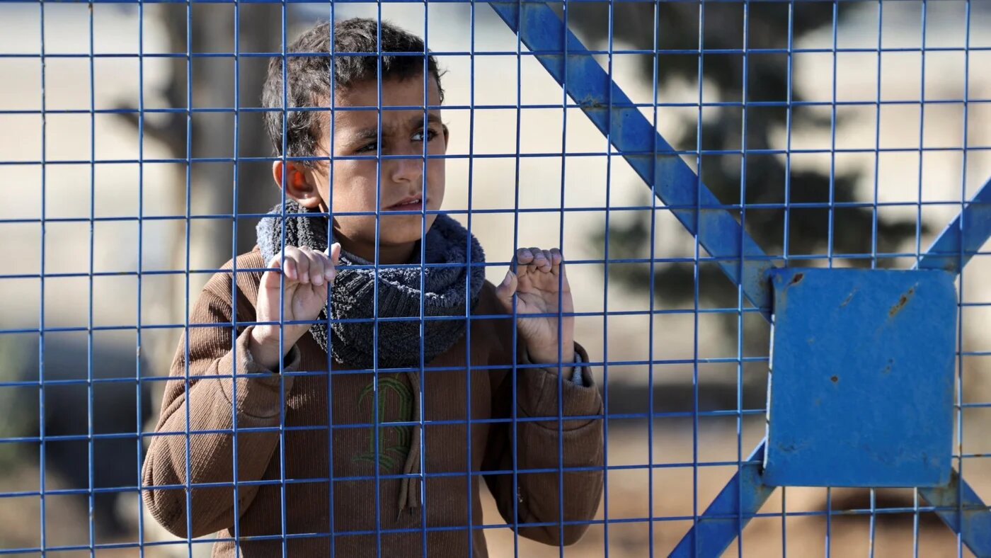 A boy, part of a group of detainees, looks through a fence at al-Hol camp after the Syrian government took control of it following the withdrawal of Syrian Democratic Forces (SDF), in Hasaka, Syria, 21 January 2026 (Reuters/Khalil Ashawi)