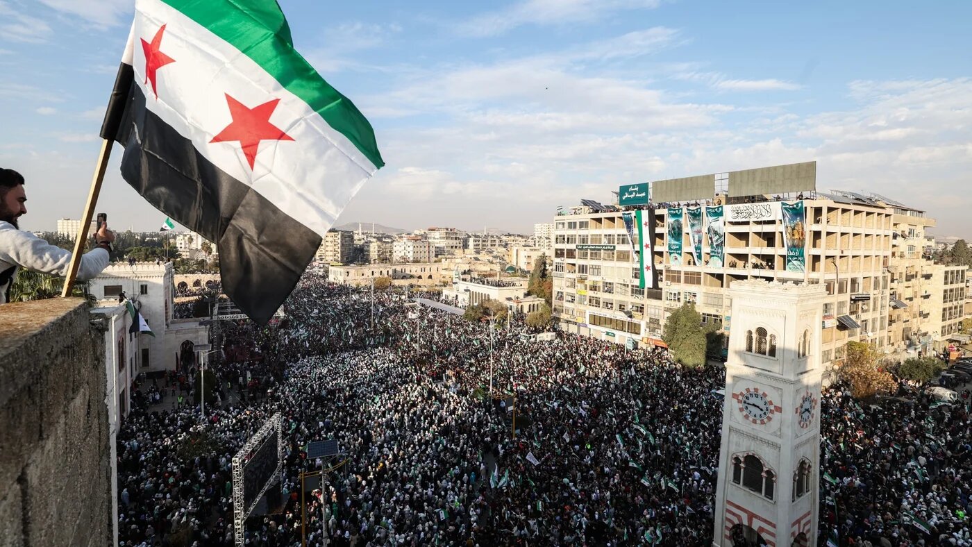 A Syrian flag flutters above crowds gathering during celebrations marking one year since a lightning offensive that eventually toppled the country's longtime ruler, in central Hama on 5 December 2025 (Omar Haj Kadour/AFP)