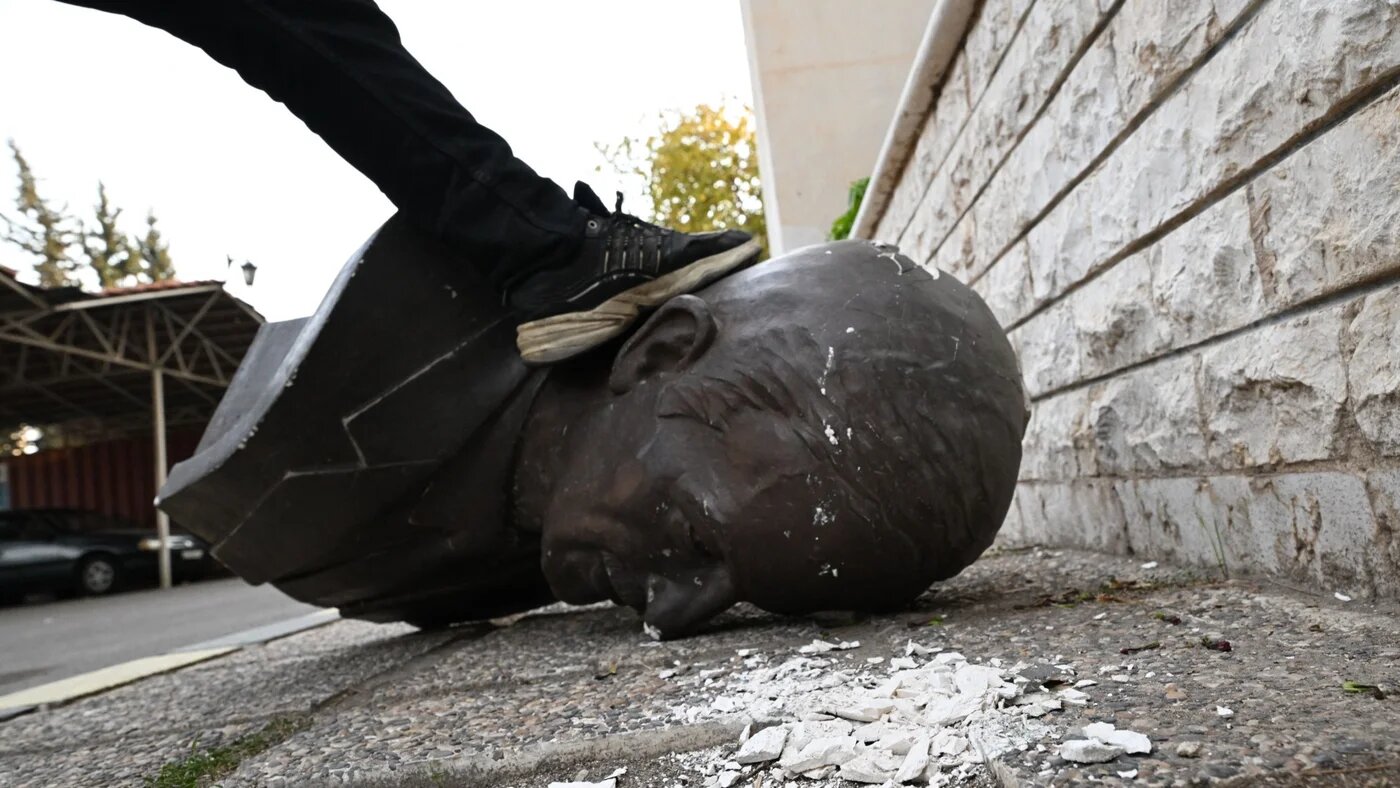 An anti-government fighter treads on a statue of late Syrian president Hafez al-Assad that was felled outside the defence ministry's military security headquarters in the Damascus district of Kafr Sousa on 9 December 2024 (AFP)