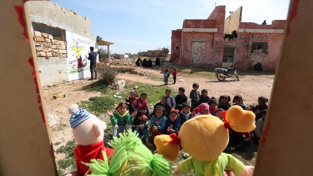 Syrian children watch a puppet show amid the ruins of buildings destroyed during Syria's civil war in the northwestern Idlib province on 30 March 2021.