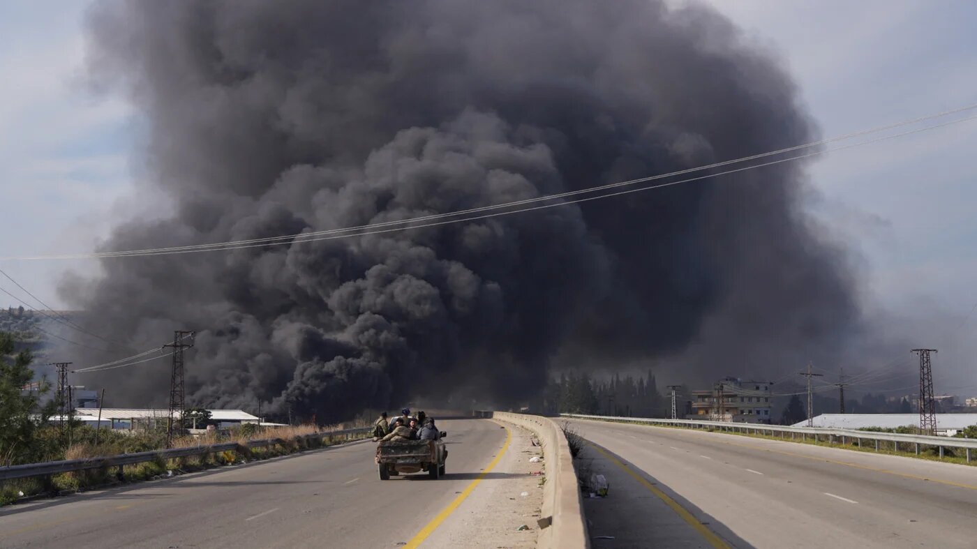 Smoke rises while members of the Syrian forces ride on a vehicle as they battle against an insurgency by fighters from ousted leader Bashar al-Assad's loyalists in Latakia on 7 March 2025 (Karam al-Masri/Reuters)