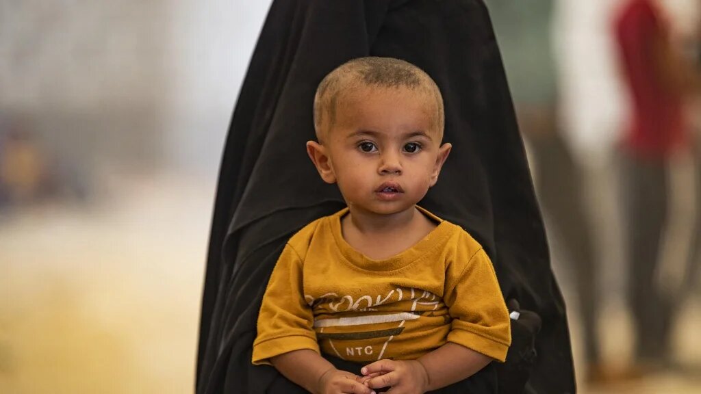 Une femme porte son enfant alors que les Syriens attendent d’être libérés du camp kurde d’al-Hol, dans le Nord-Est du gouvernorat d’Hassaké, le 14 août 2022 (AFP/Delil Souleiman)