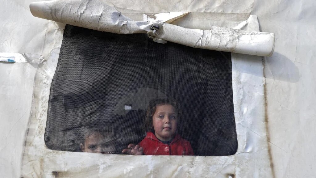 Des petits Syriens regardent par la fenêtre d’une fenêtre de tente, dans un abri d’urgence, au nord de la province d’Idleb, tenue par les rebelles, un jour après les séismes qui ont frappé la Turquie et la Syrie (AFP/Abdulaziz Ketaz)