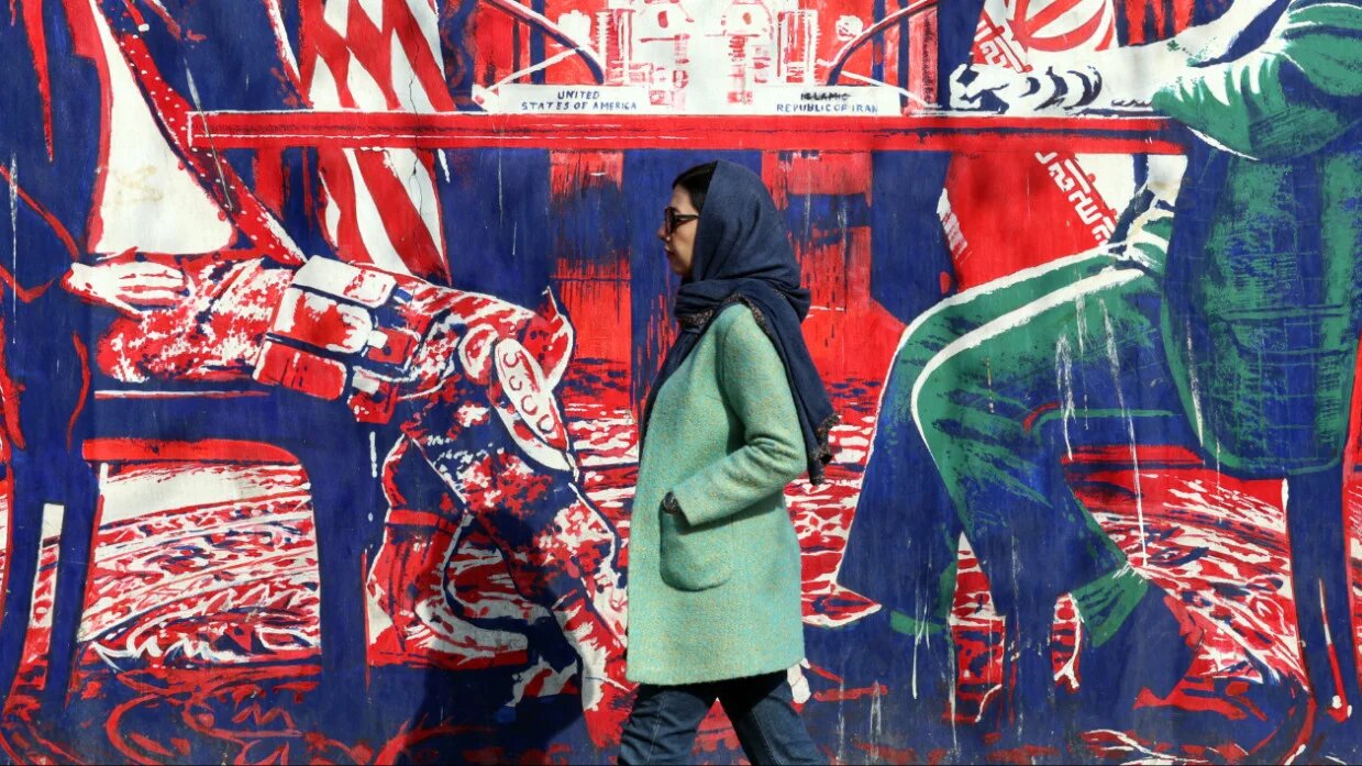 An Iranian woman walk past anti-US mural depicting Iran and US negotiation table, painted on the outer walls of the former US embassy, in Tehran on 6 February 2026 (AFP)
