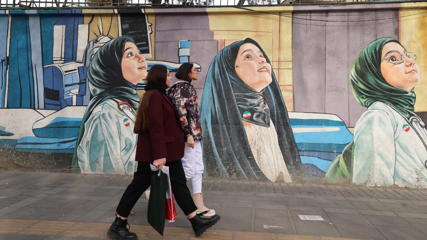 Women walk past a mural depicting children as future scientists in Tehran on 3 February 2026 (AFP)