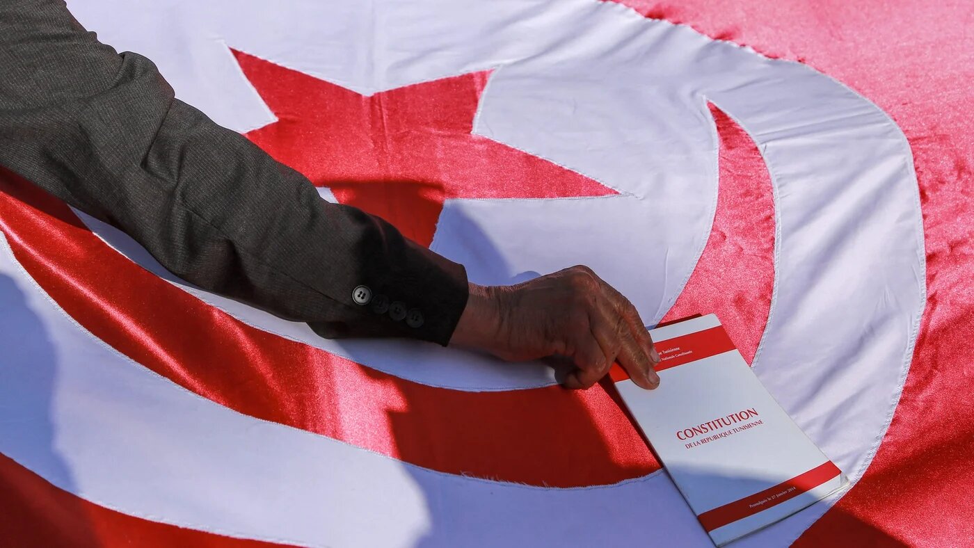 A man places a copy of the Tunisian constitution atop a Tunisian national flag during a demonstration called against President Kais Saied on 13 February 2022 (AFP)
