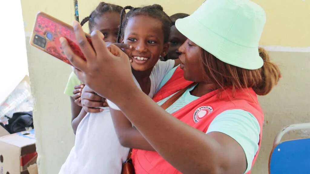 Une membre du Croissant-Rouge tunisien prend un selfie avec de jeunes migrants qui ont fui les violences à Sfax (est) vers la zone tampon militarisée entre la Tunisie et la Libye, et ont été accueillis dans un internat de Ben Guerdane, le 12 juillet 2023 (AFP/Fathi Nasri)