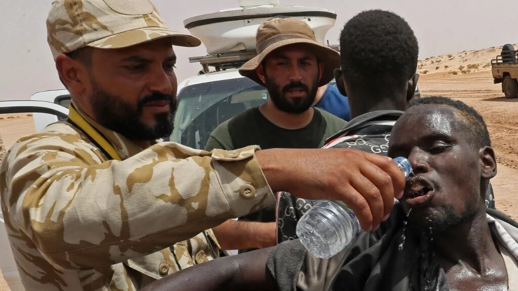 Des gardes-frontières libyens fournissent de l’eau aux migrants d’origine africaine déportés par les autorités tunisiennes à la frontière Libye-Tunisie, le 30 juillet 2023 (AFP/Mahmoud Turkia)