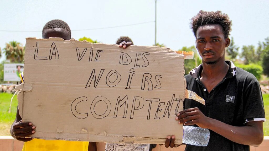 Des migrants subsahariens tiennent une pancarte lors d’une manifestation contre les conditions désastreuses des migrants dans la ville de Sfax en Tunisie, le 7 juillet 2023 (AFP/Houssem Zouari)
