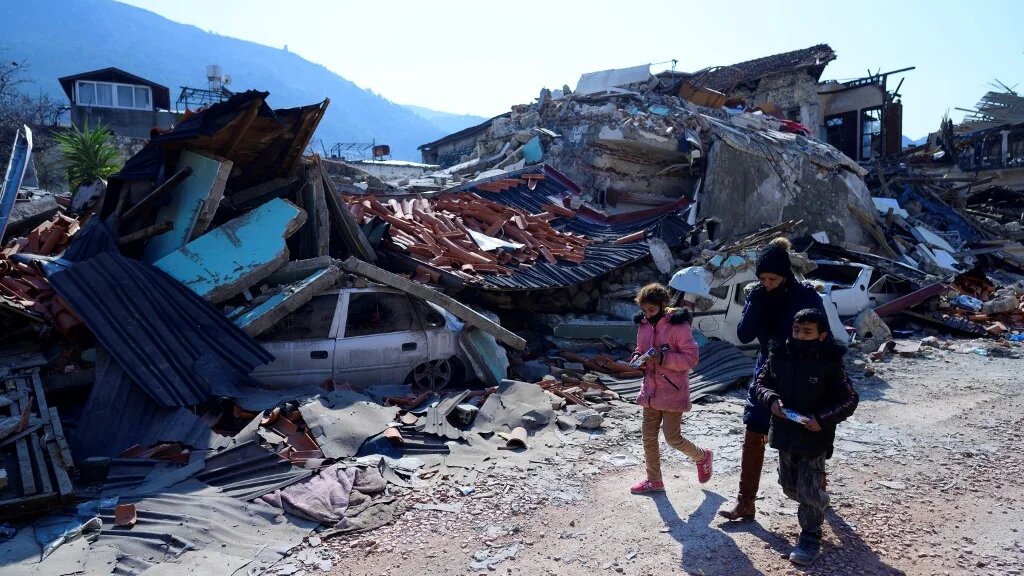 Des rescapés marchent à côté des ruines causées par le puissant séisme à Antakya, au sud de la Turquie (AFP/Yasin Akgul)