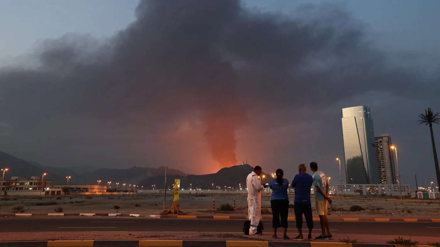 Foreign workers look at a tall plume of black smoke rising after an explosion in the Fujairah industrial zone in the UAE on 3 March 2026 (Fadel Senna/AFP)