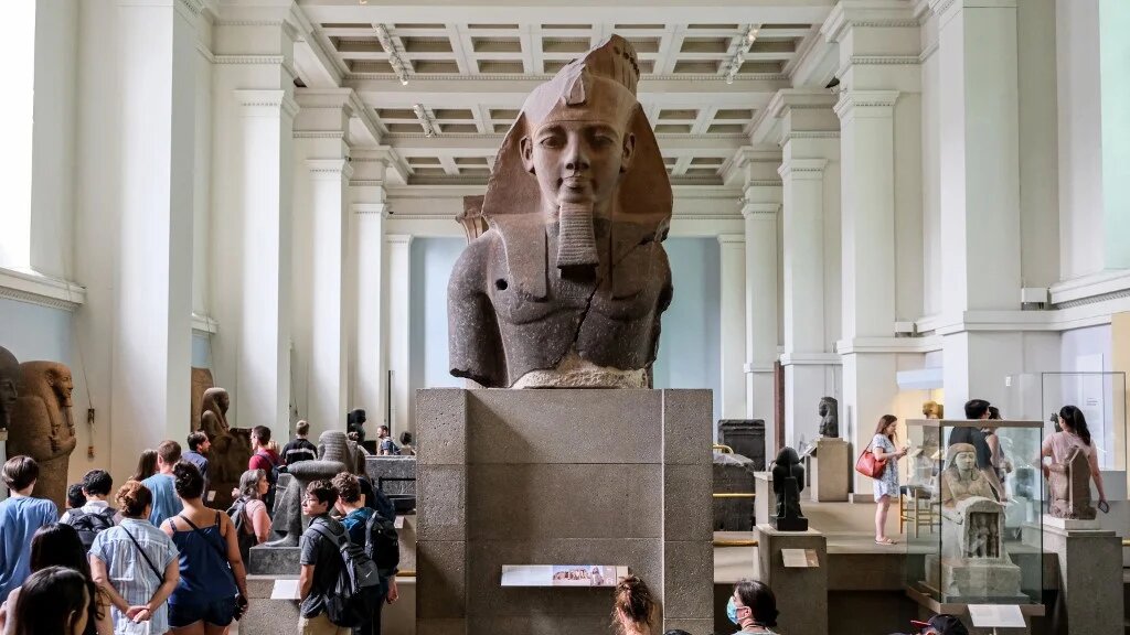 Visitors look at the Egyptian “Younger Memnon” colossal granite head statue, on display at the British Museum in London, on 23 July 2022 (Amir Makar/AFP)