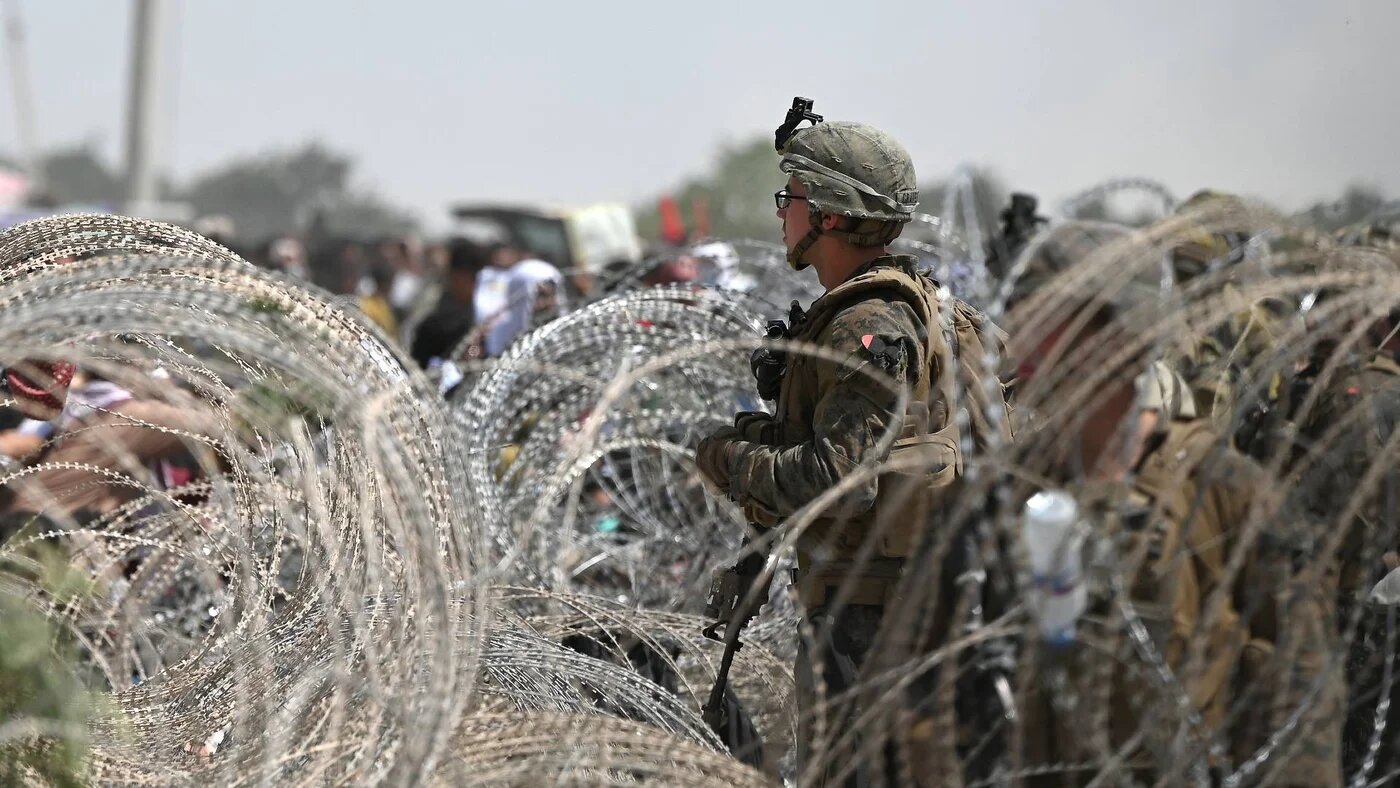 A US soldier stands on guard as Afghans gather on a roadside near the military part of the airport in Kabul on 20 August 2021.