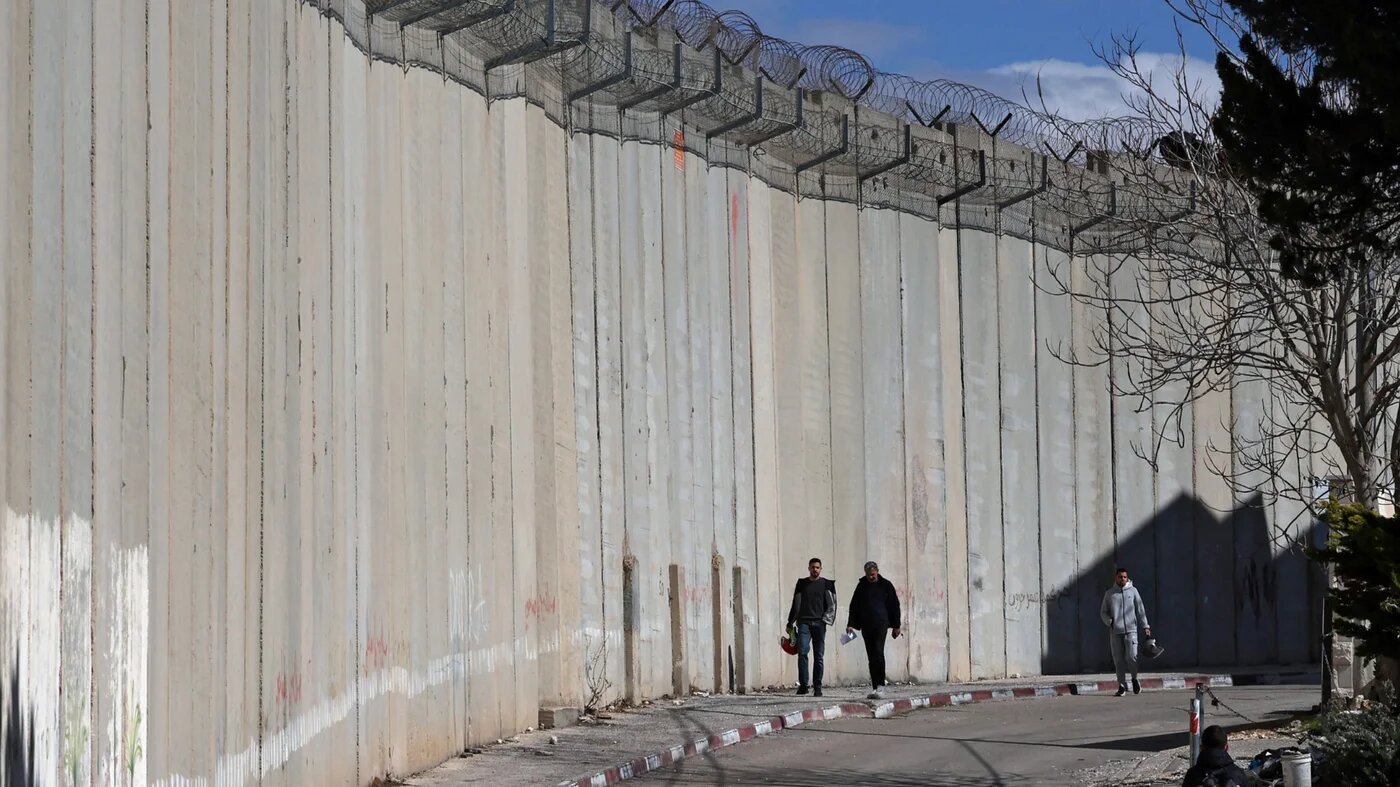 Palestinians walk alongside Israel's controversial separation barrier in the Dahiat al-Barid suburb of occupied East Jerusalem on 24 February 2026 (AFP)