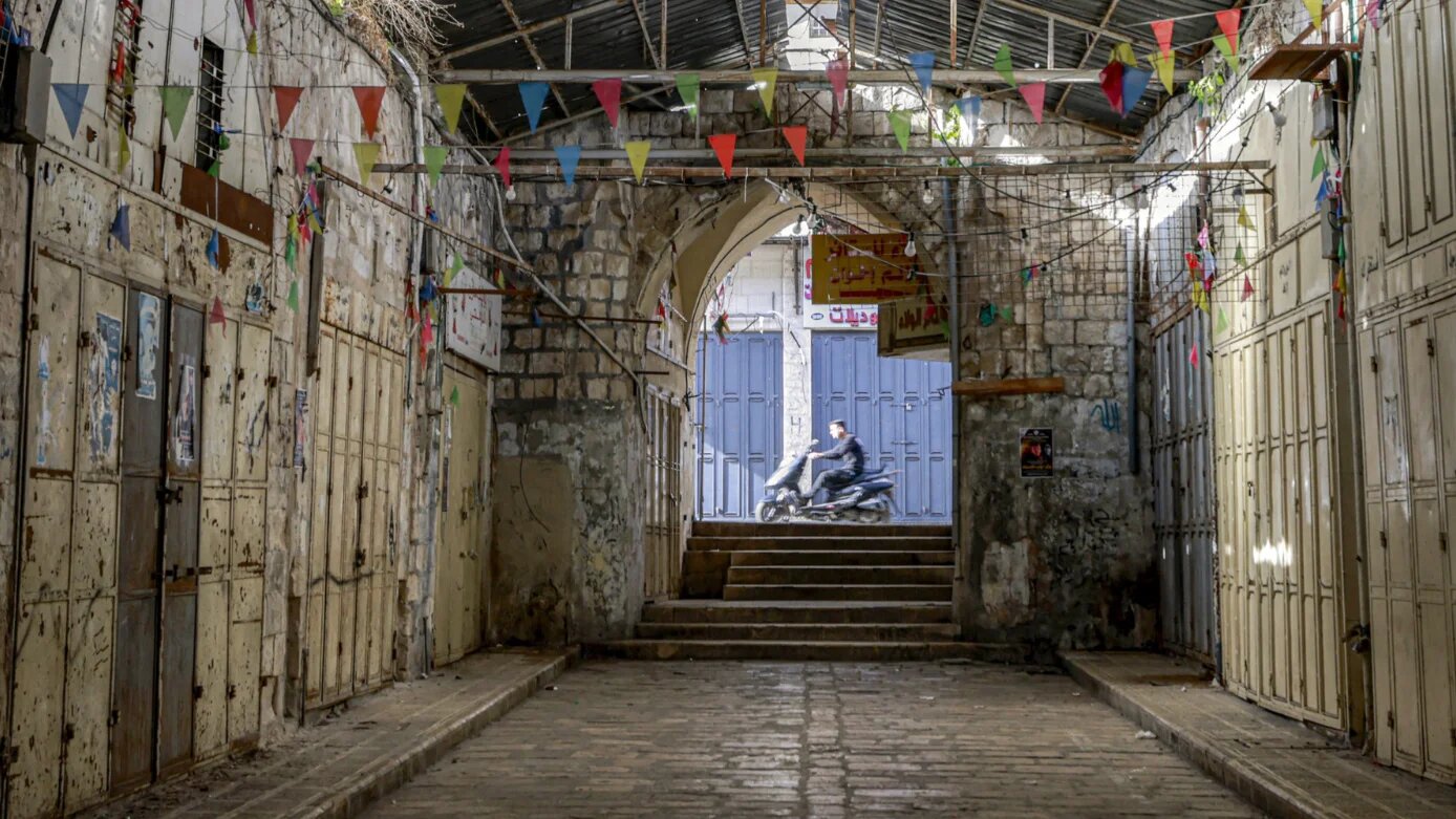 A man rides a motorcycle past an alley with shuttered shops during a general strike in the occupied West Bank city of Nablus on 7 April 2025 (Jaafar Ashtiyeh/AFP)