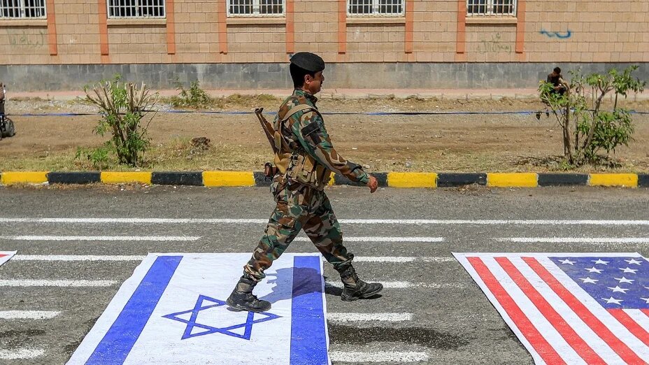 A fighter loyal to Yemen’s Houthi movement walks over depictions of the Israeli and US flags during a demonstration in Sanaa on 22 July 2026 (Mohammed Huwais/AFP)
