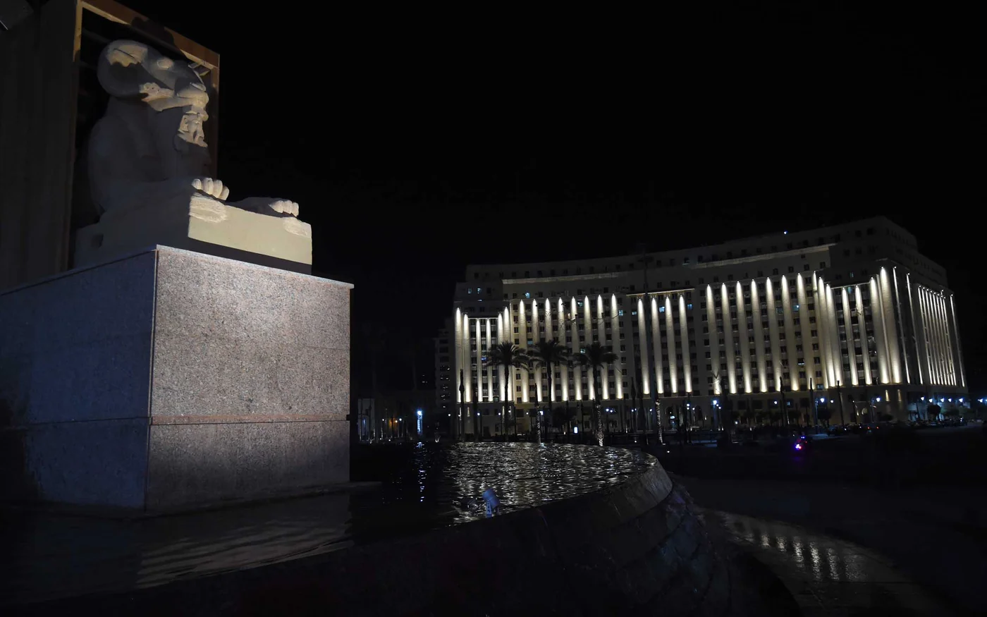 Vue nocturne de la place, avec l’un des sphinx à tête de bélier. La façade du Mogamma al-Tahrir est illuminée par le nouveau système d’éclairage (MEE)